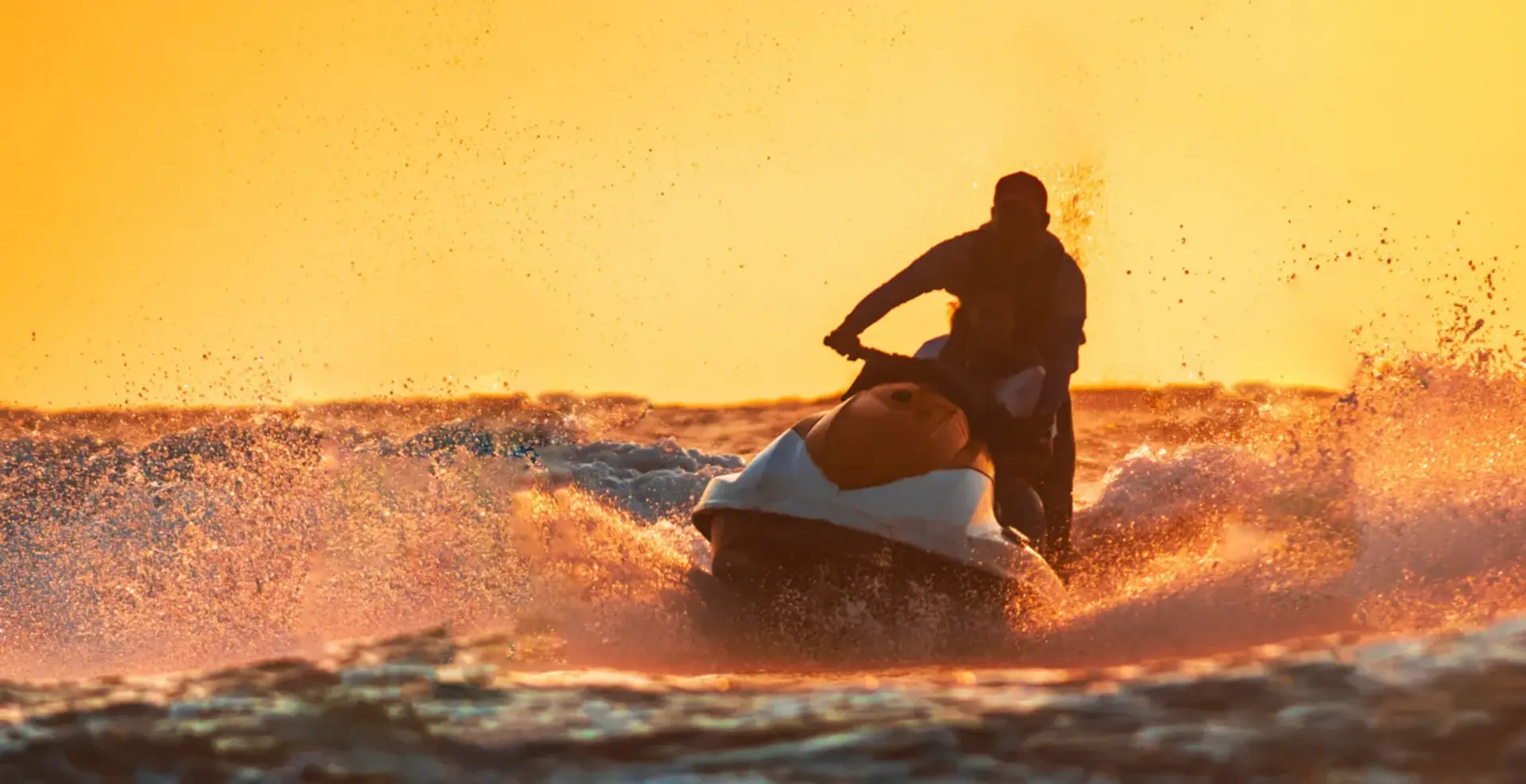 A jet ski running across a wave at sunset